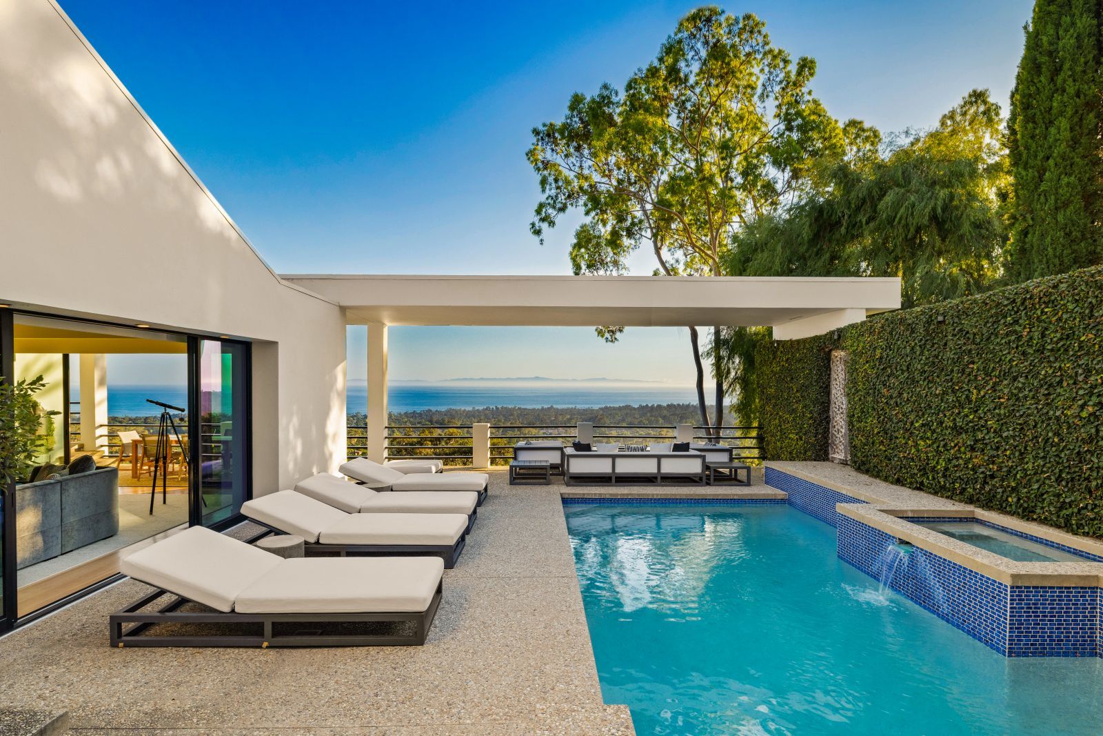 An aqua blue ocean view plunge pool lined with luxury lounge chairs outside of a white modernist home